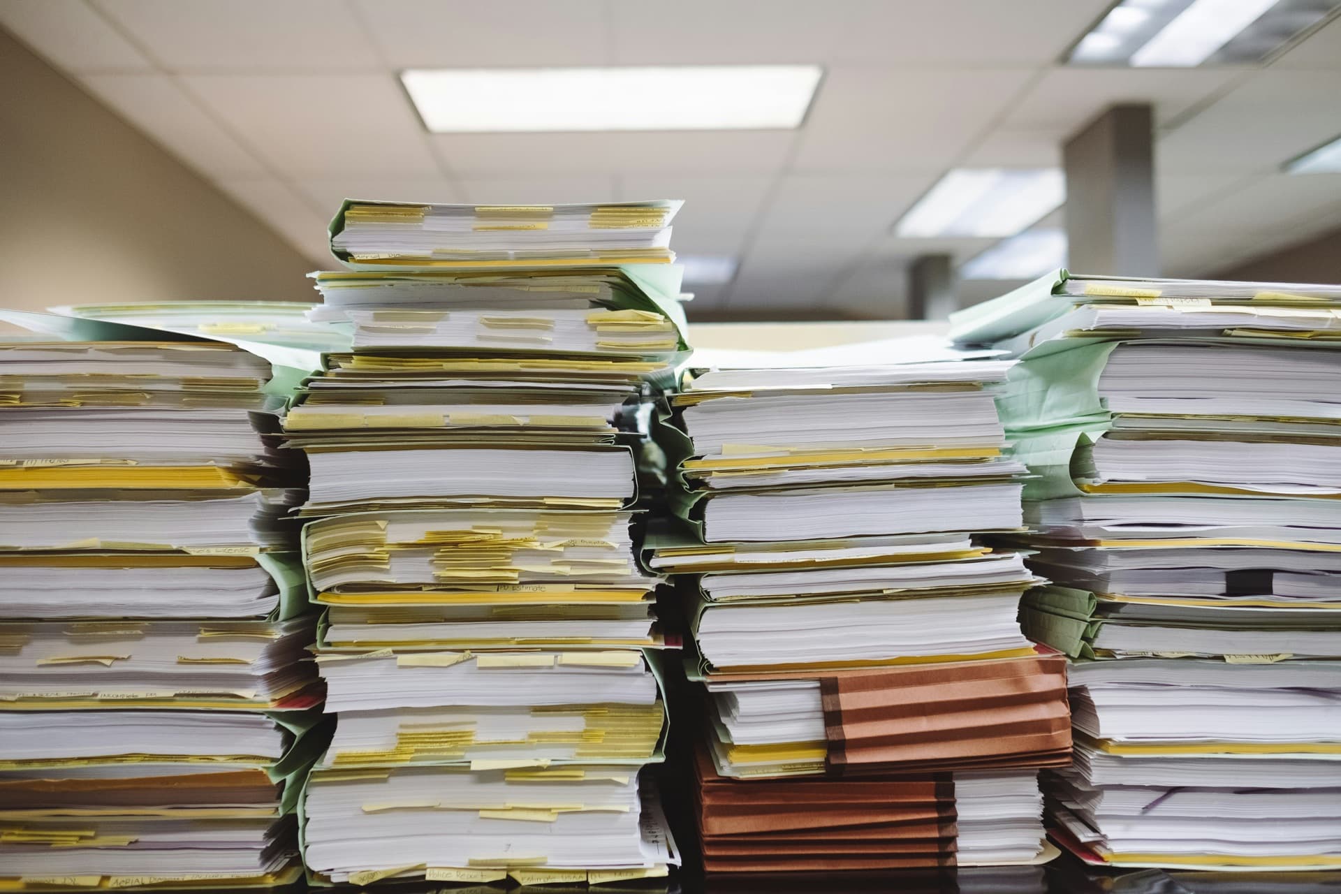 Towering stacks of paperwork and tabbed files piled on an office desk